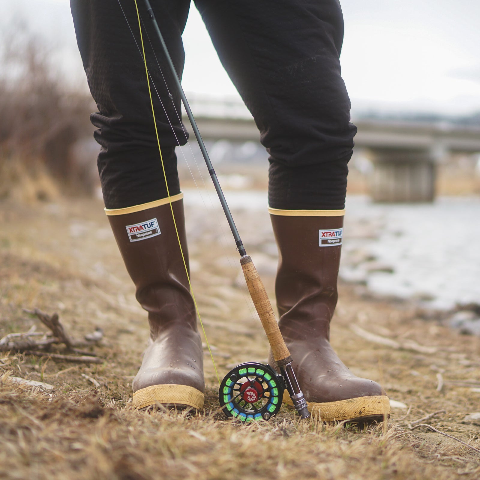 An angler wearing tall brown boots beside the shore.